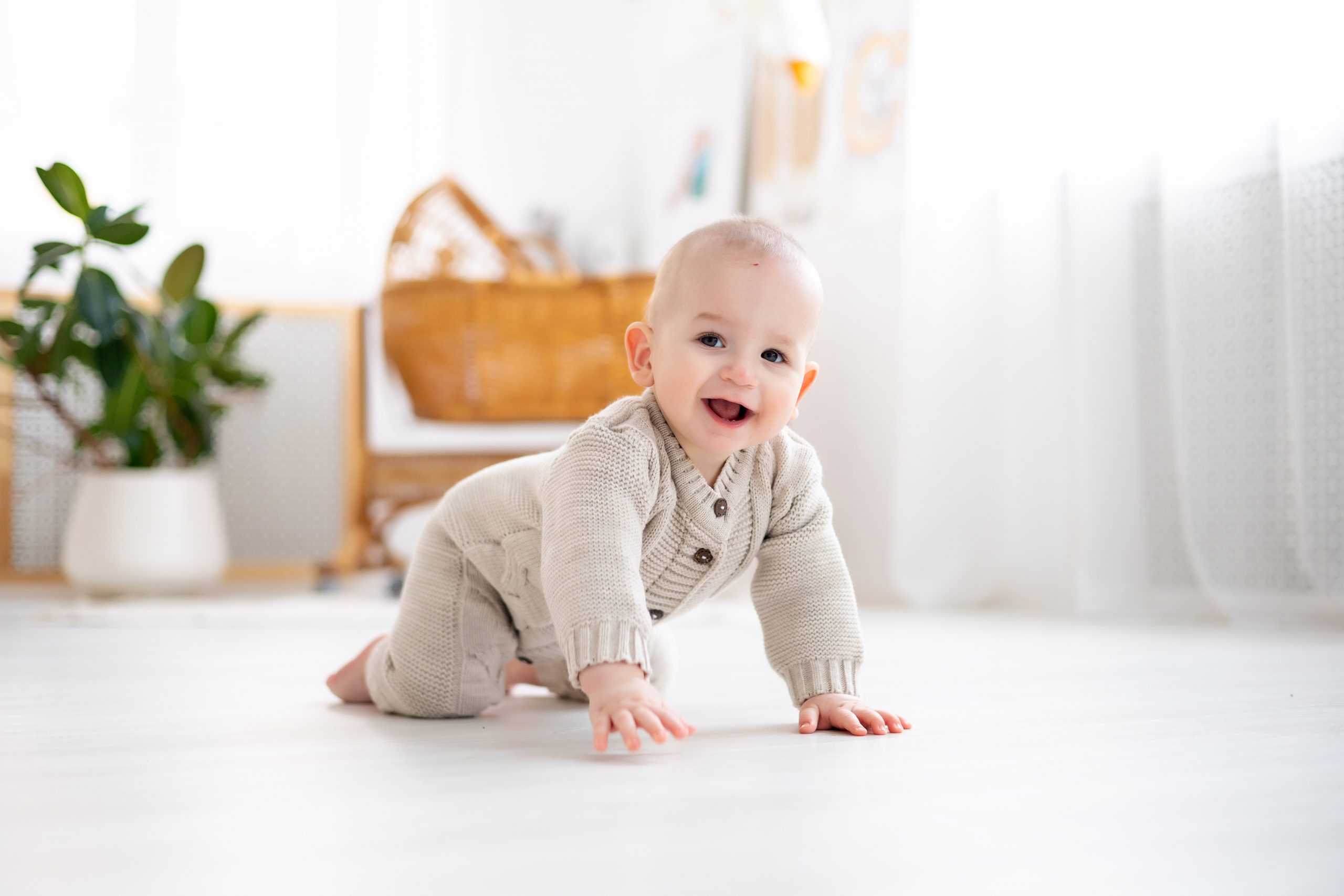 cute little baby boy in a pastel wool knitted suit learning to crawl on the floor in a bright living room, baby smiling, playing, early development of children Montessori zu Hause
